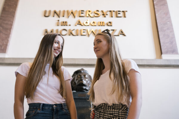 Dwie dziewczyny stojące obok popiersia Adama Mickiewicza. W tle napis: Uniwersytet imienia Adama Mickiewicza